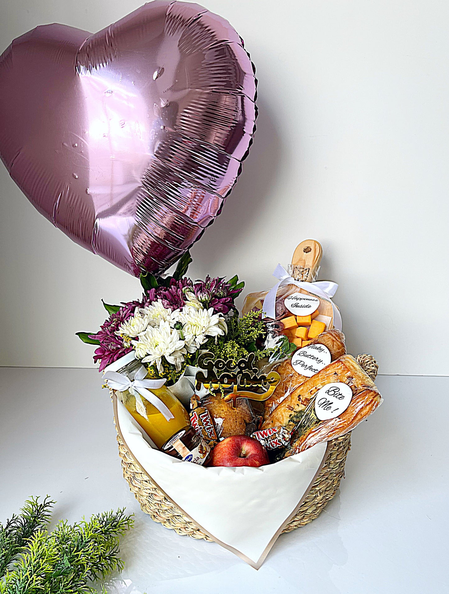 Heart-shaped gift basket with flowers, snacks, and a balloon on a white background