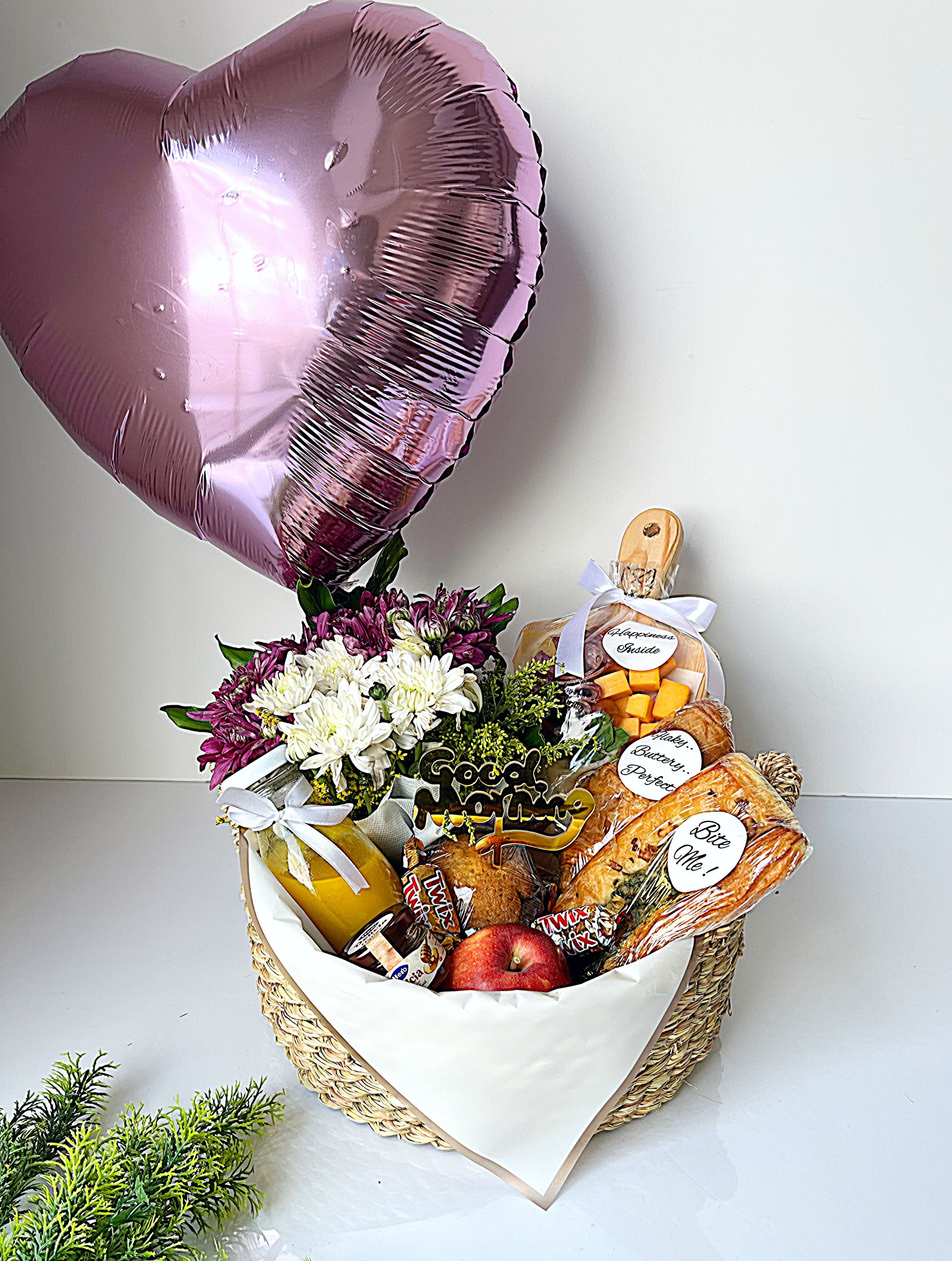 Heart-shaped gift basket with flowers, snacks, and a balloon on a white background