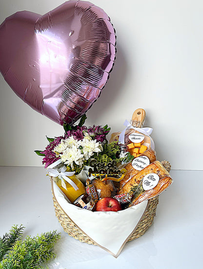Heart-shaped gift basket with flowers, snacks, and a balloon on a white background