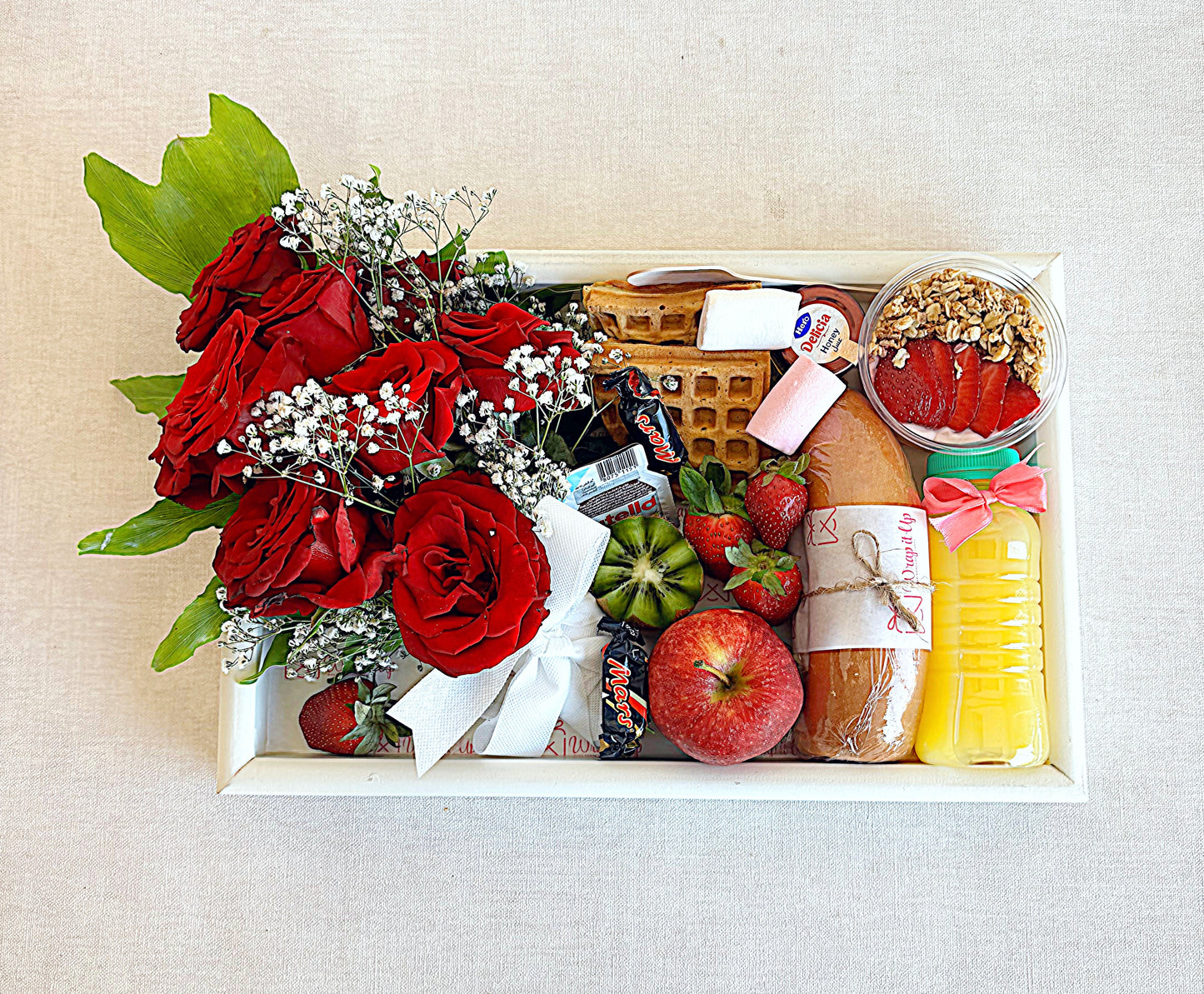 Gift box with red roses, fruits, and a loaf of bread on a light background