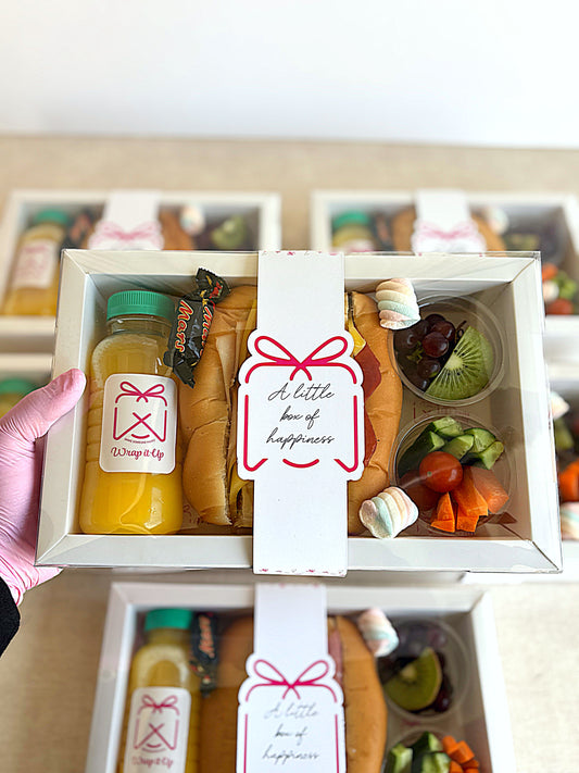Gift box with food items and a card labeled 'A little box of happiness' held by a hand.