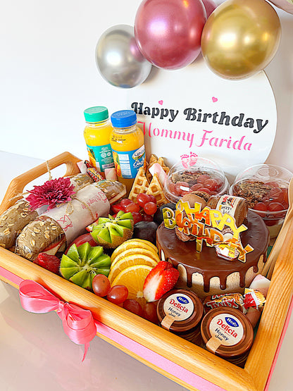 Birthday gift tray with cake, fruits, and snacks on a white background