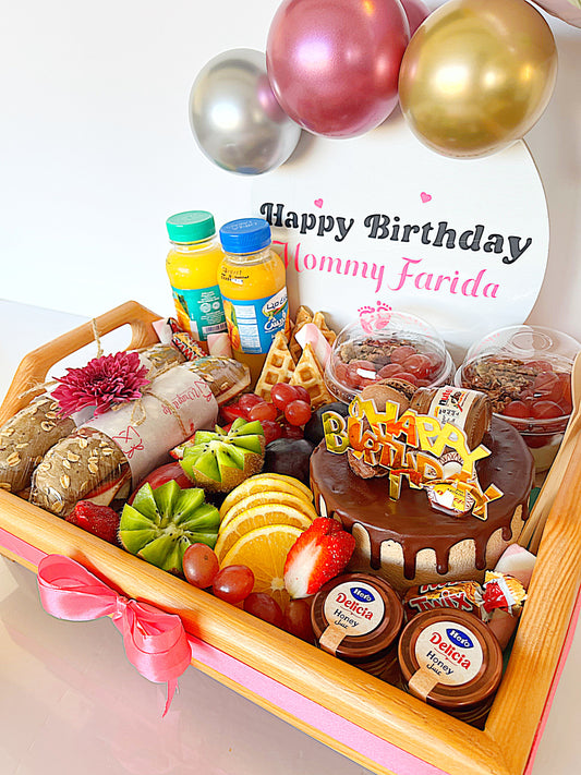 Birthday gift tray with cake, fruits, and snacks on a white background