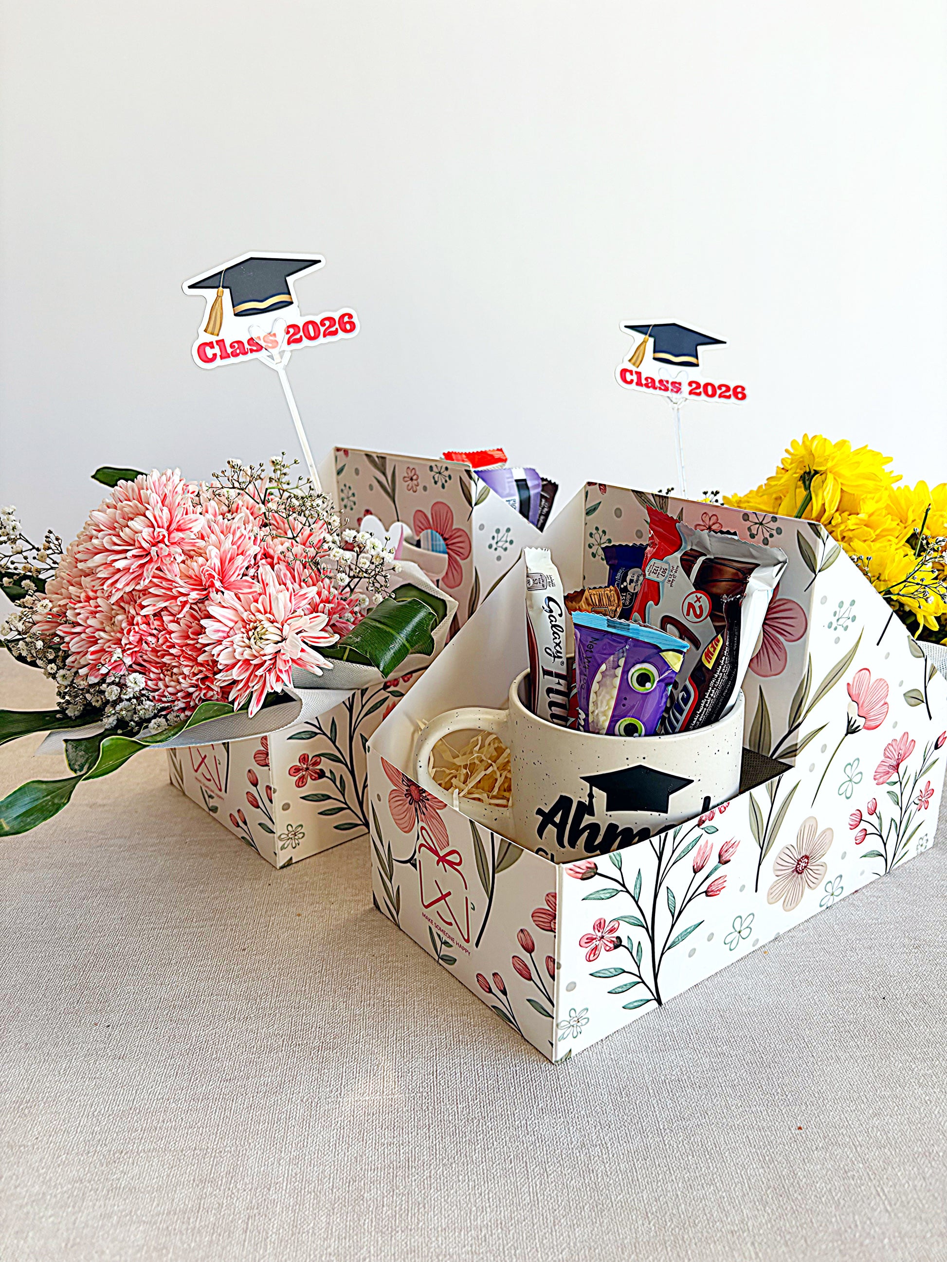 Graduation-themed gift basket with flowers, mugs, and decorative items on a light background