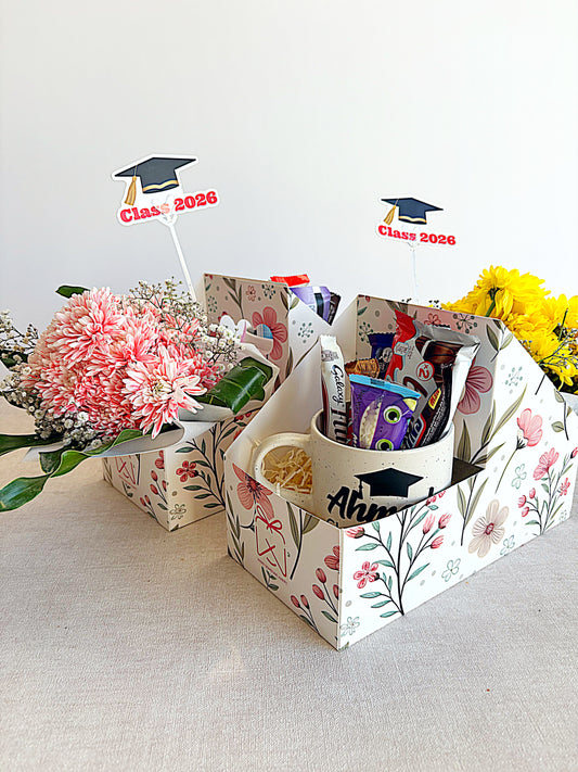 Graduation-themed gift basket with flowers, mugs, and decorative items on a light background