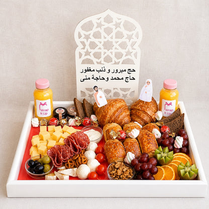 Tray of assorted foods including bread, fruits, and cheeses with a decorative chair in the background.