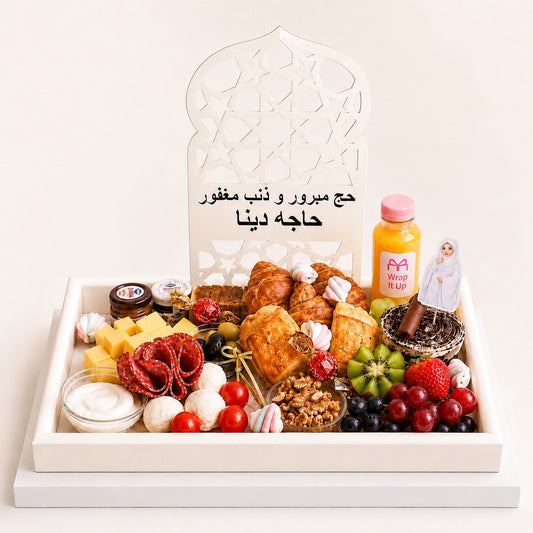 Assorted food items and a bottle of juice in a decorative box with Arabic text on a white background